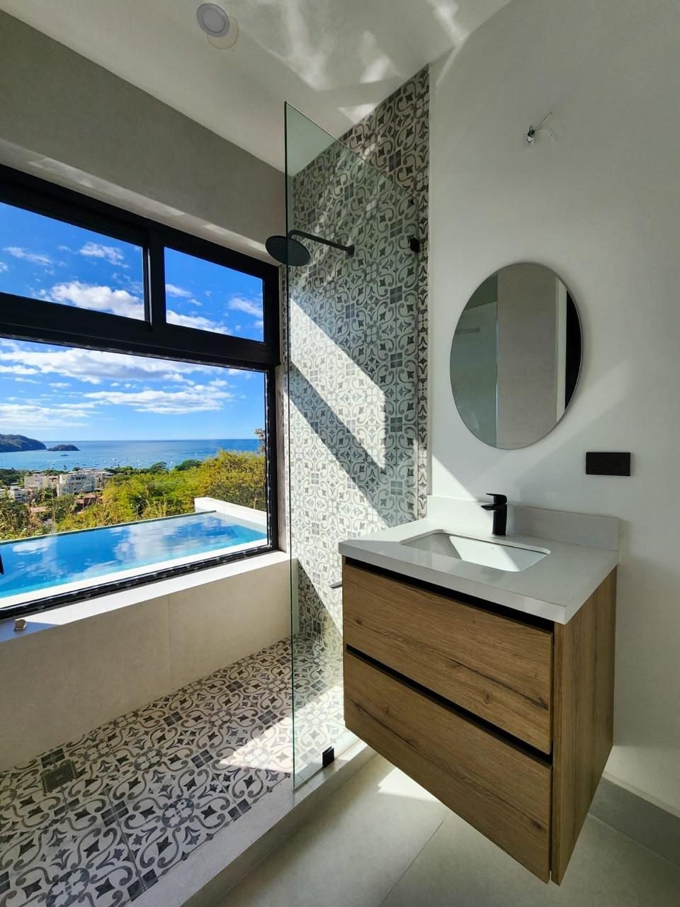 Baño con ventana de perfil negro hacia el mar y mampara de vidrio templado