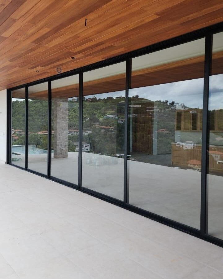 Corrediza de gran formato de perfil negro bajo un cielo de madera, con vista a la montaña