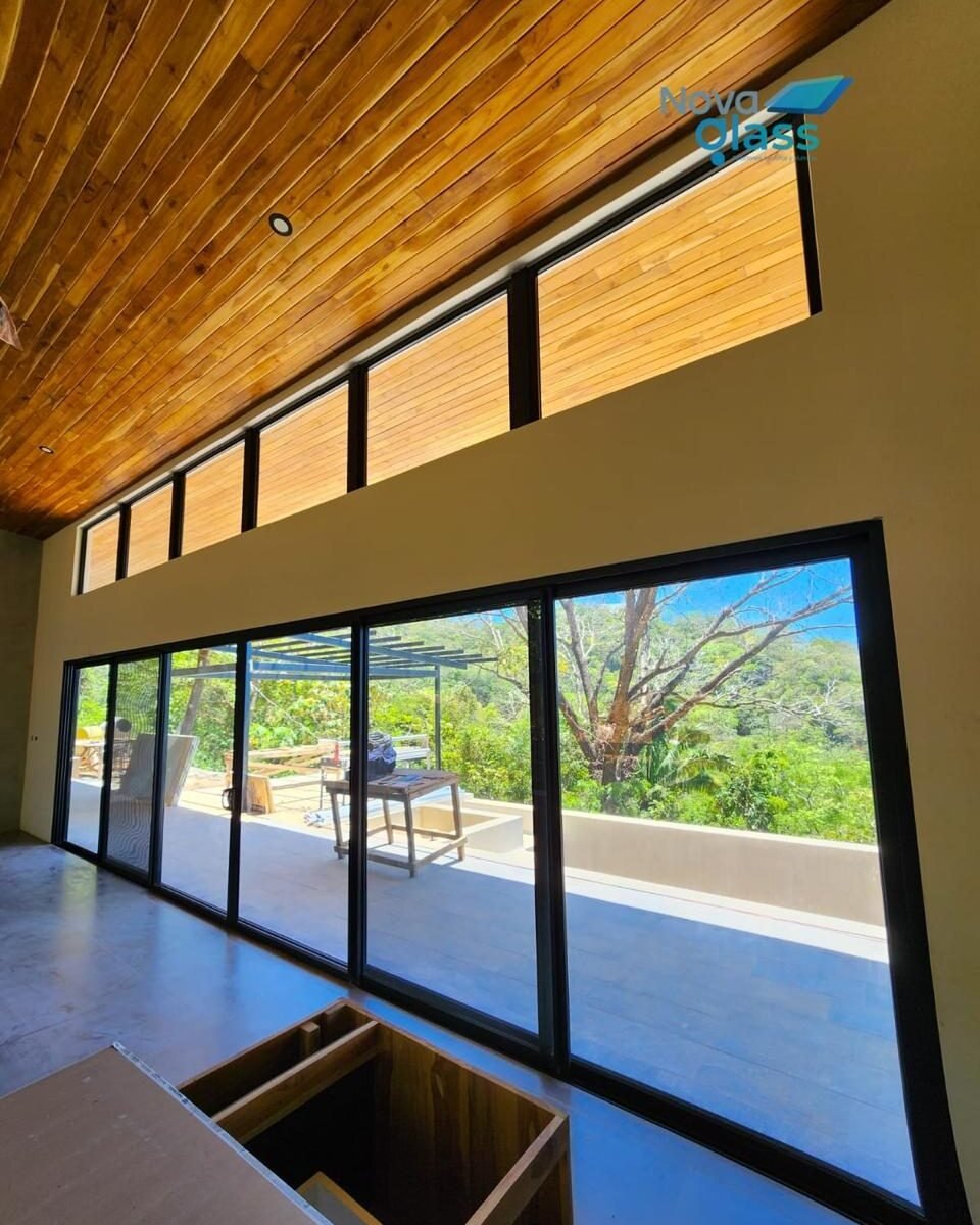 Corrediza de gran formato y ventanas altas de perfil negro hacia una terraza con árboles