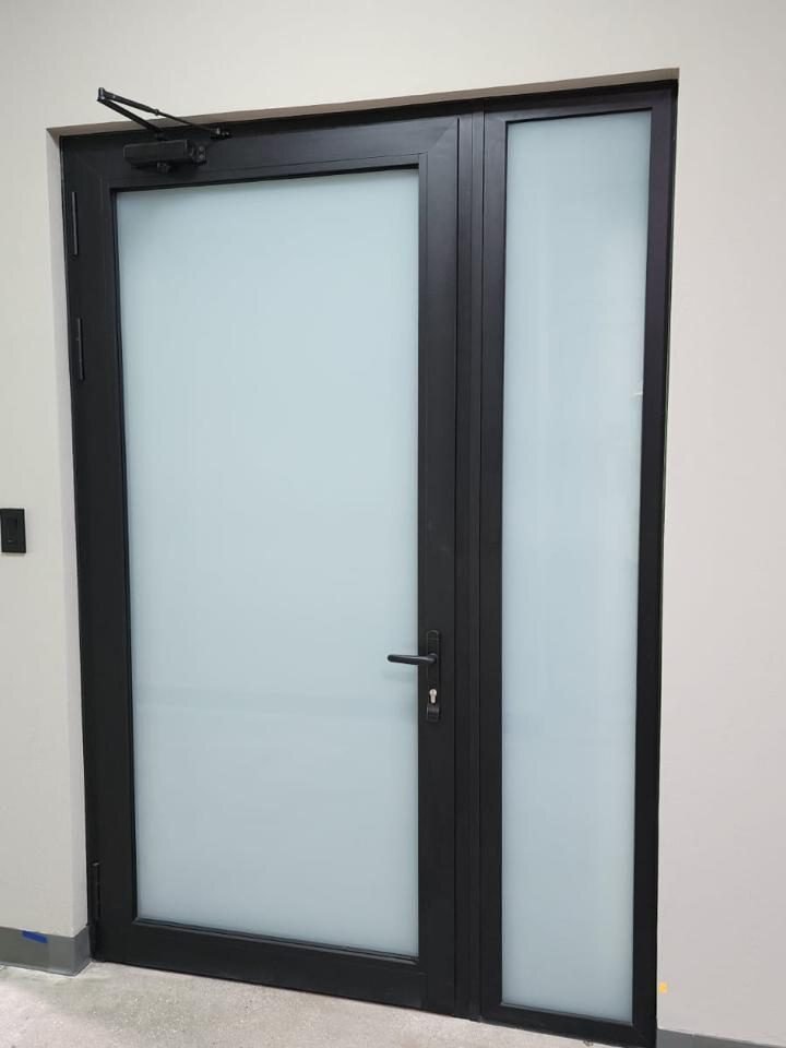 Puerta de aluminio negro con vidrio esmerilado y panel lateral fijo